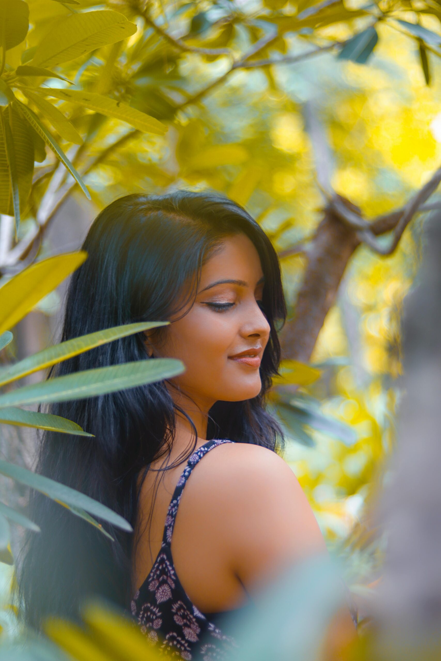 A serene portrait of a woman amidst lush green foliage in daylight.